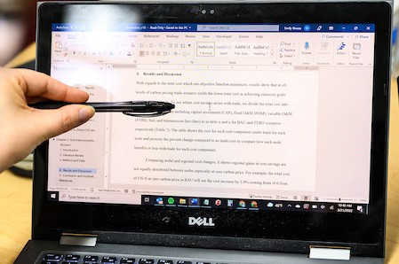Someone uses a pen to point to lines of text on a computer screen